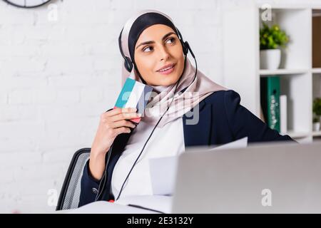 smiling arabian interpreter in headphones holding digital translator with uae flag symbol, blurred foreground Stock Photo