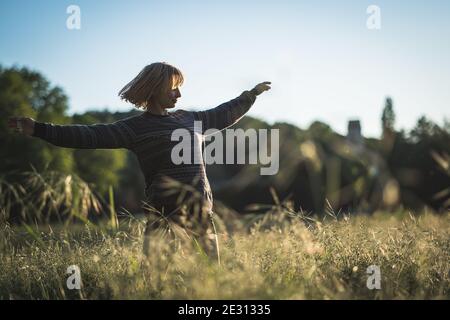 A young woman dancing in tall grass during golden hour Stock Photo