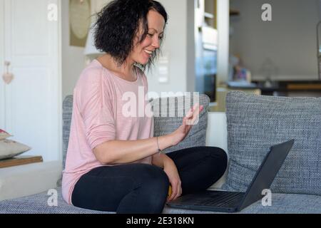 Side view of a woman waving with her hand to the computer while doing home office during the Covid-19 pandemic lockdown Stock Photo