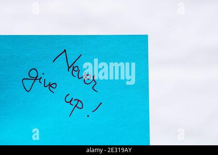Never give up handwriting text close up isolated on blue paper with copy space. Writing text on memo post reminder Stock Photo