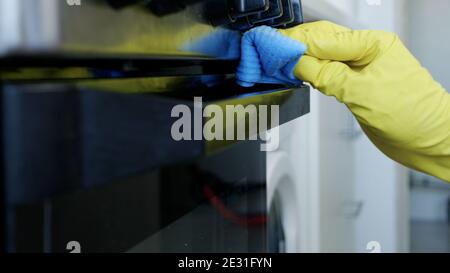 Closeup Image with Person Hands Wearing Protective Yellow Household Gloves in the Kitchen and Cleaning a Stove