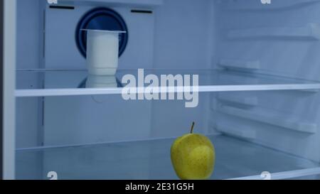 One Cold Yogurt and One Fresh Apple in an Empty Fridge in the Kitchen Stock Photo