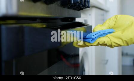 Closeup Image with Person Hands Wearing Protective Yellow Household Gloves in the Kitchen and Cleaning a Stove Stock Photo