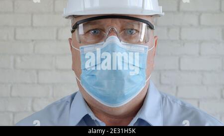 Engineer Portrait Wearing Hardhat, Protective Eyeglasses and Medical Face Mask in Coronavirus Pandemic Stock Photo