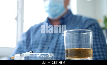 Image with a Man who Drinks Alcohol and Smokes a Cigarette Wearing Protective Mask on His Face Stock Photo