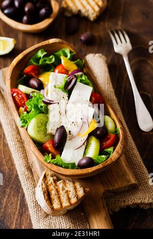 Greek salad in wooden plate on old wooden background. Traditional Greek dish. Selective focus. Top view. Stock Photo