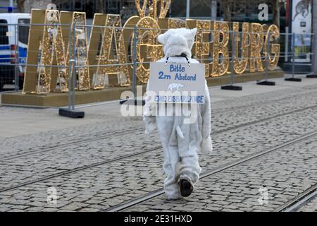 16 January 2021, Saxony-Anhalt, Magdeburg: A participant of the Fridays for Future movement stands during a demonstration under the motto 'FFF against Right - For Climate Justice' in a polar bear costume at the main station next to the lettering 'Magdeburg' from the world of lights that had been set up before Christmas. On his back he carries a sign 'Please 2 m distance - one polar bear length'. Due to the measures to contain the coronavirus, the traditional events are cancelled, so there are many smaller rallies in the state capital to mark the 76th anniversary of the destruction of Magdeburg Stock Photo