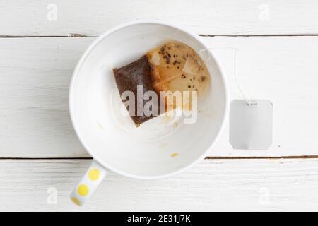 Closeup empty cup with used tea bag on white wooden table. Top view. Stock Photo
