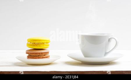 A cup of coffee and two macaroons lemon and chocolate on white wooden table. Front view Stock Photo