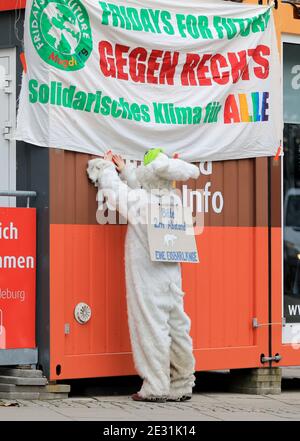 Magdeburg, Germany. 16th Jan, 2021. A participant of the Fridays for Future movement hangs up a poster at the central station during a demonstration under the motto 'FFF against the right - for climate justice' in a polar bear costume. On his back he carries a sign 'Please 2 m distance - a polar bear length'. Due to the measures to contain the coronavirus, the traditional events are cancelled, so there are many smaller rallies in the state capital to mark the 76th anniversary of the destruction of Magdeburg on 16 January 1945. Credit: Peter Gercke/dpa-Zentralbild/dpa/Alamy Live News Stock Photo