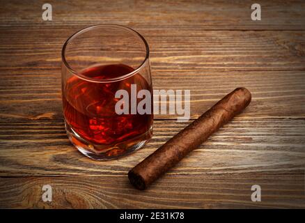 Glass of whiskey with ice cubes and cigar on a wooden table. Vignette Stock Photo