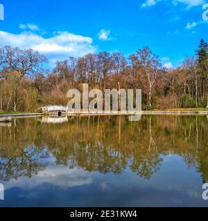 Cow Pond and Baroque-style footbridge with diamond lattice balustrade. Lake surrounded by trees reflected in the water. Windsor Great Park, Berkshire. Stock Photo