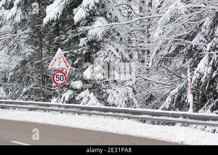 slippery road with snow covered traffic signs in winter, speed limit 50 and attention traffic light Stock Photo