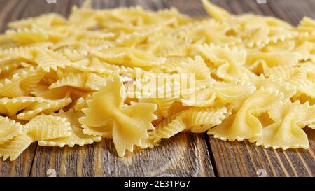 Pasta in the shape of a bow-tie on wooden table. Stock Photo