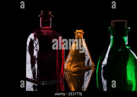 Still life of three colored decorative bottles with corks on glass against black background. Stock Photo