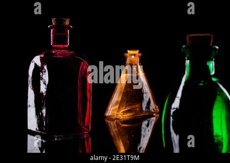 Still life of three colored decorative bottles with corks on glass against black background. Stock Photo