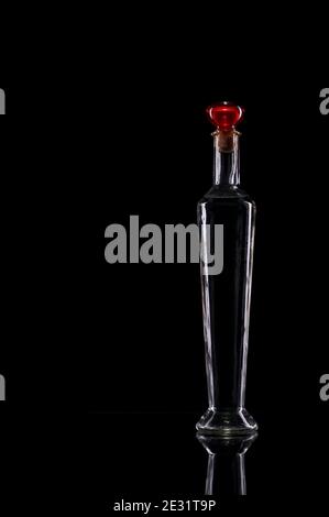 Still life of slim decorative bottles with red cap on glass against black background. Stock Photo