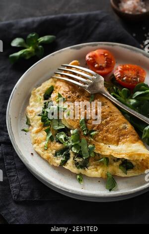 Stuffed omelette with tomatoes, red bell pepper, cream cheese and corn or lamb's lettuce on dark wooden background with copy space. Healthy diet food Stock Photo