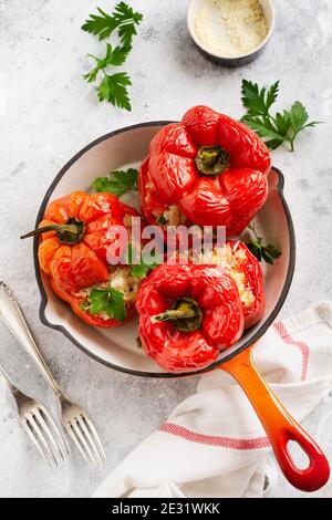 Red bell peppers stuffed with rice and vegetables on cast iron pan on gray concret background. Stock Photo