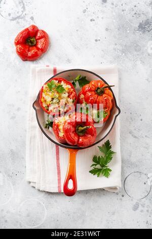 Red bell peppers stuffed with rice and vegetables on cast iron pan on gray concret background. Stock Photo