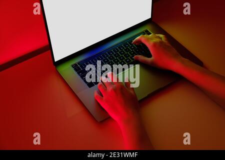 Female hands on a modern laptop keyboard in brightly lit red background Stock Photo