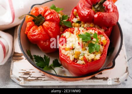 Red bell peppers stuffed with rice and vegetables on cast iron pan on gray concret background.