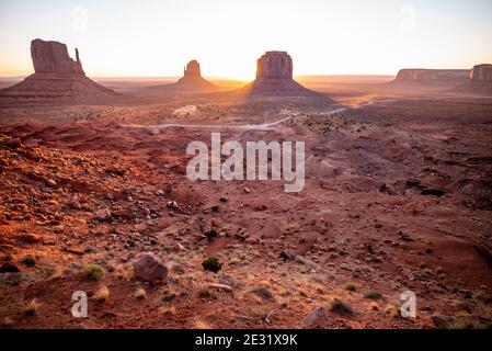 The West Mitten, East Mitten and Merrick Butte rock formations and road at sunrise in Monument Valley Navajo Tribal Park, Arizona and Utah, USA Stock Photo