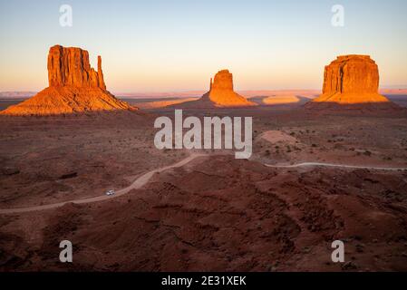 The famous West Mitten, East Mitten and Merrick Butte rock formations at sunset, and a car on the winding road. Monument Valley, Arizona and Utah, USA Stock Photo