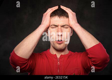 A man holds his head with his hand on a dark background. Headache, migraine, stress Stock Photo