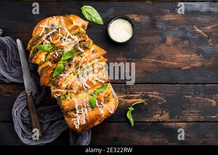 Pull-apart bread with Italian pasta pesto, basil and parmesan cheese in baking form over old dark concrete background. Top view. Rustic stile. Stock Photo