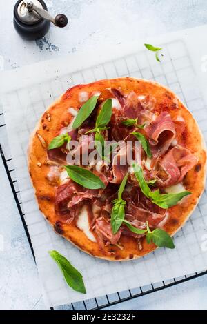 Homemade pizza with jamon, mozzarella and fresh basil leaves on a light concrete old background. Top view. Stock Photo