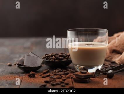 Glass of Irish cream baileys liqueur with coffee beans and powder with dark chocolate on dark wood background. Space for text Stock Photo