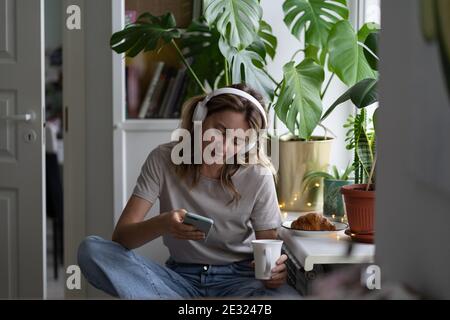 Woman listening to music wear headphones, using mobile phone chatting in social networks, drink tea Stock Photo