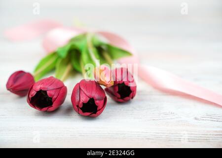 Five red tulips with a ribbon lie on a light wooden background. Side view, with space to copy. Stock Photo