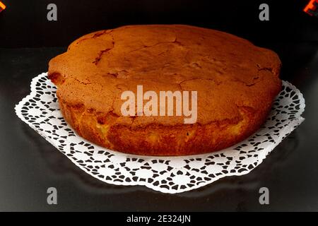 Homemade sponge cake on a white lace paper and a black background. Stock Photo