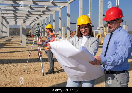Young Female Architect and Construction Engineer Checking the Blueprint on Construction Site. Gender Equality at Work. Man and Woman in Hardhats. Stock Photo