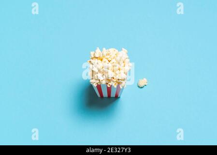 Above view with a popcorn box isolated on a blue-colored background. Homemade popcorn in a striped box. High angle view minimalist with popcorn flakes Stock Photo