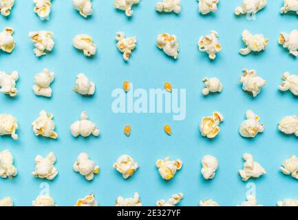 Pattern with popcorn flakes and unpopped corn aligned symmetrically on a seamless blue background. Pattern with popcorn and corn seeds, above view. Stock Photo