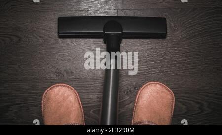 Male feet in room slippers with a vacuum cleaner, cleaning the house with a vacuum cleaner, a young man bends and cleaning the laminate. Housekeeping. Stock Photo
