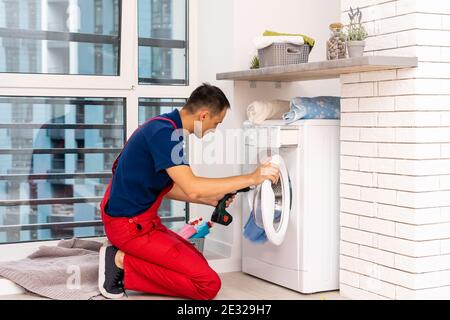 male adult repairman with tool and clipboard checking washing machine in bathroom Stock Photo