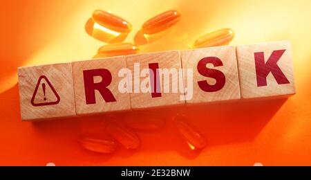 Risk Word on Wooden Cubes and oil capsules pills around on orange background. Medical healthcare concept. Stock Photo