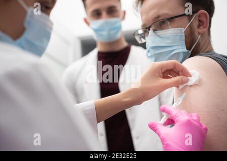 The doctor shows the medical trainee how to properly make the vaccine. The young adult is vaccinated against COVID19. An injection with a new vaccine formulation against COVID19 and other infectious diseases. Stock Photo
