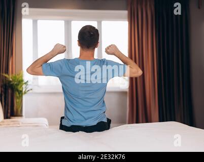 Good morning Young man waking up in bed and stretching his arms, back view, copy space. Stock Photo