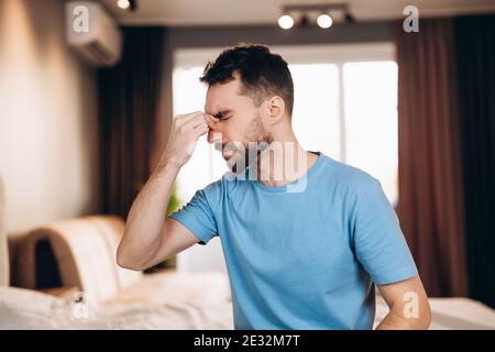 Man with beard sitting in bed at home suffering from headache or hangover. Bedtime and rest concept Stock Photo