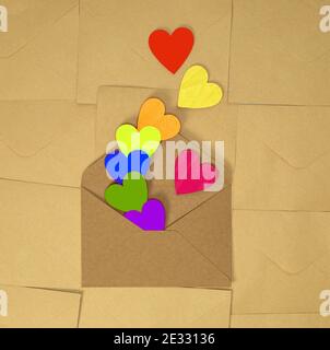 Brown craft paper envelope with various rainbow colorful hearts on plain brown background texture top view, Valentines Day, romantic concept copy Stock Photo