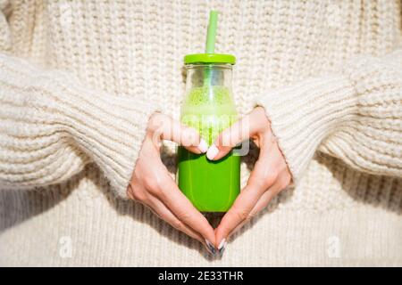 Healthy heart. Woman in woollen sweater holding bottle with green homemade detox smoothie or juice. Healthy body, life, eating, living concept Stock Photo