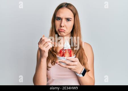 Young blonde woman eating strawberry ice cream depressed and worry for distress, crying angry and afraid. sad expression. Stock Photo
