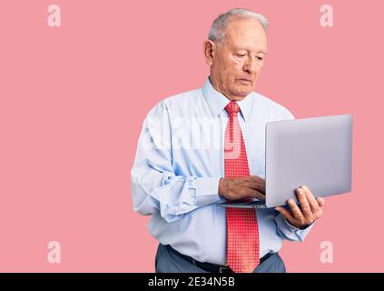 Senior handsome grey-haired man wearing tie using laptop thinking attitude and sober expression looking self confident Stock Photo