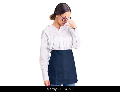 Beautiful brunette young woman wearing professional waitress apron tired rubbing nose and eyes feeling fatigue and headache. stress and frustration co Stock Photo