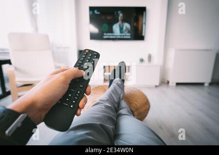 Man sitting on sofa and watching TV with remote controller in his hand. Rest at home. Stock Photo